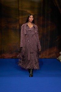 Naomi Campbell portant un trench en viscose mélangée à imprimé baroque de couleur rouge Duchess, un jodhpur en coton coloris marron Treacle et beige Pebble, et des bottes en cuir dans la teinte gris Anchor.