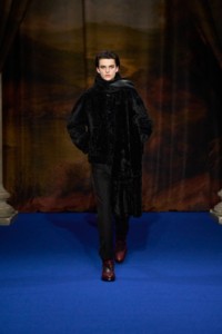 Tristan Watkins in einer schwarzen Lammfelljacke mit Schaldetail, einem schwarzen Oberteil aus Alpakawolle im Rippstrick, einer eleganten Wollhose im Schwarzton Panther und Jodhpurstiefeln „Ledger“ aus Leder im Lilaton Rubus