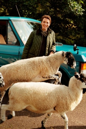 Olivia Colman hinter einer Schafherde, gekleidet in eine Steppjacke von Burberry und Hemd im Burberry Check-Karomuster