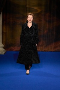 Lesley Manville usando trench coat de veludo com estampa padronizada Vine em jacquard, calças de alfaiataria pretas e scarpins Cameo em xadrez Burberry Check na cor marrom Brush.