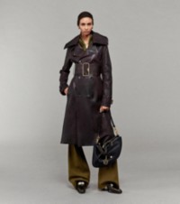 Modelo usando um trench coat de couro com patchwork e calças de alfaiataria, segurando uma bolsa Shield Twin de couro média