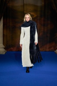 Jean Campbell usando vestido branco com lantejoulas, botas Cavalier de couro pretas, brincos de argola Charm folheados a ouro, anel Star Collage folheado à prata e cachecol de shearling em cinza azulado.