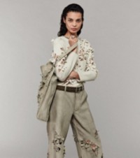 Model wearing Daisy Cutout Sweater and Suede Trousers, holding Daisy Cutout Small Shield Twin Tote Bag