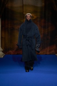 Sope Dirisu wearing cashmere shawl collar coat in pier melange grey, sunflower jacquard silk pyjama shirt in silhouette black, corduroy tailored trousers in twilight blue, low boots in black and leather pouch in storm blue.