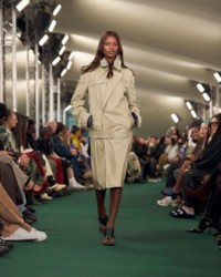 A modelo está usando um trench coat de couro com sandálias Bay.