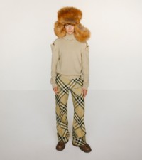 Model in einem Pullover mit Druckknöpfen in der Farbe Hunter und einer Wollhose in Flachsfarben mit Reißverschlussdetails.