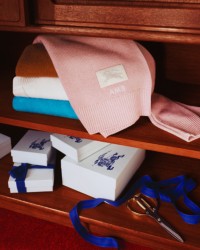 Photo d'un portefeuille et d'un porte-cartes Burberry posés sur une table en bois, avec un tiroir ouvert rempli d'écharpes Burberry Check