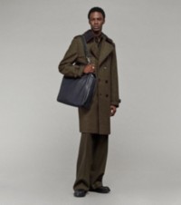 Modelo usando um trench coat em tweed com calças de alfaiataria e segurando uma bolsa tote Shield Twin pequena
