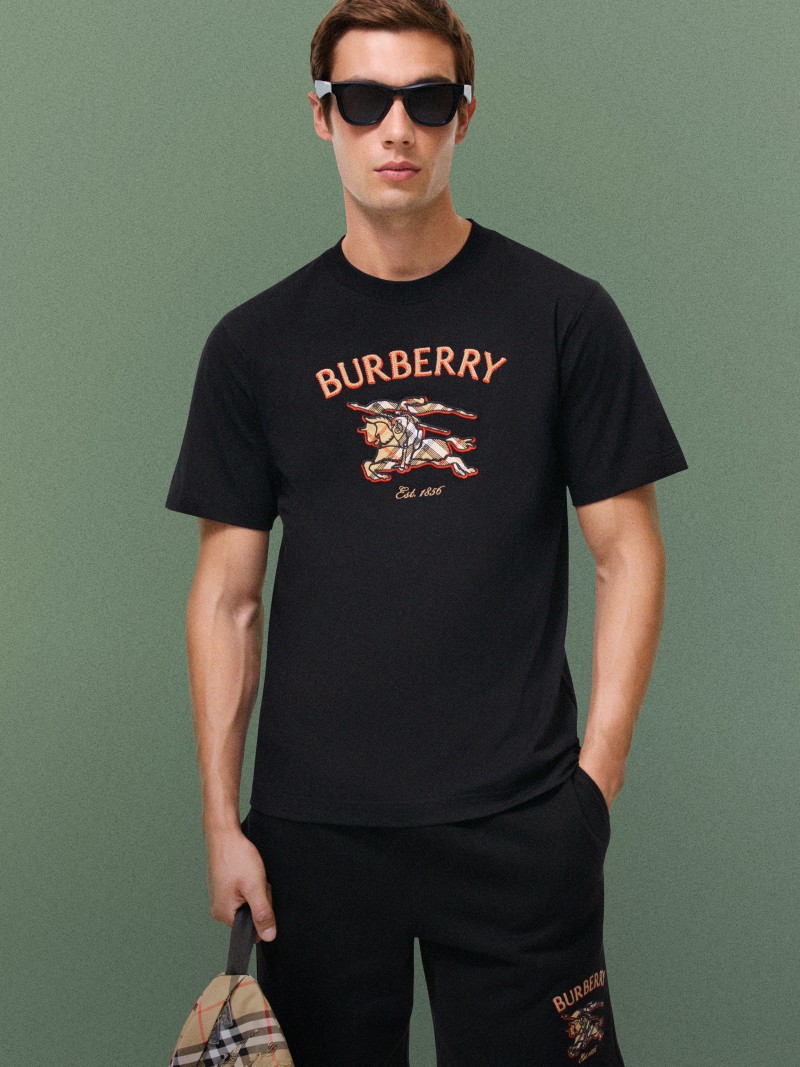 Person wearing dark sunglasses and a black graphic T-shirt featuring Burberry branding.