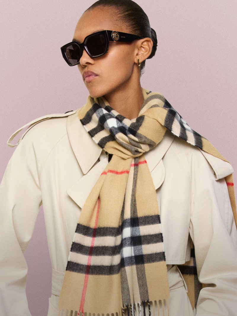 Person wearing oversized sunglasses, a light-coloured trench coat and a Burberry beige check-pattern cashmere scarf.