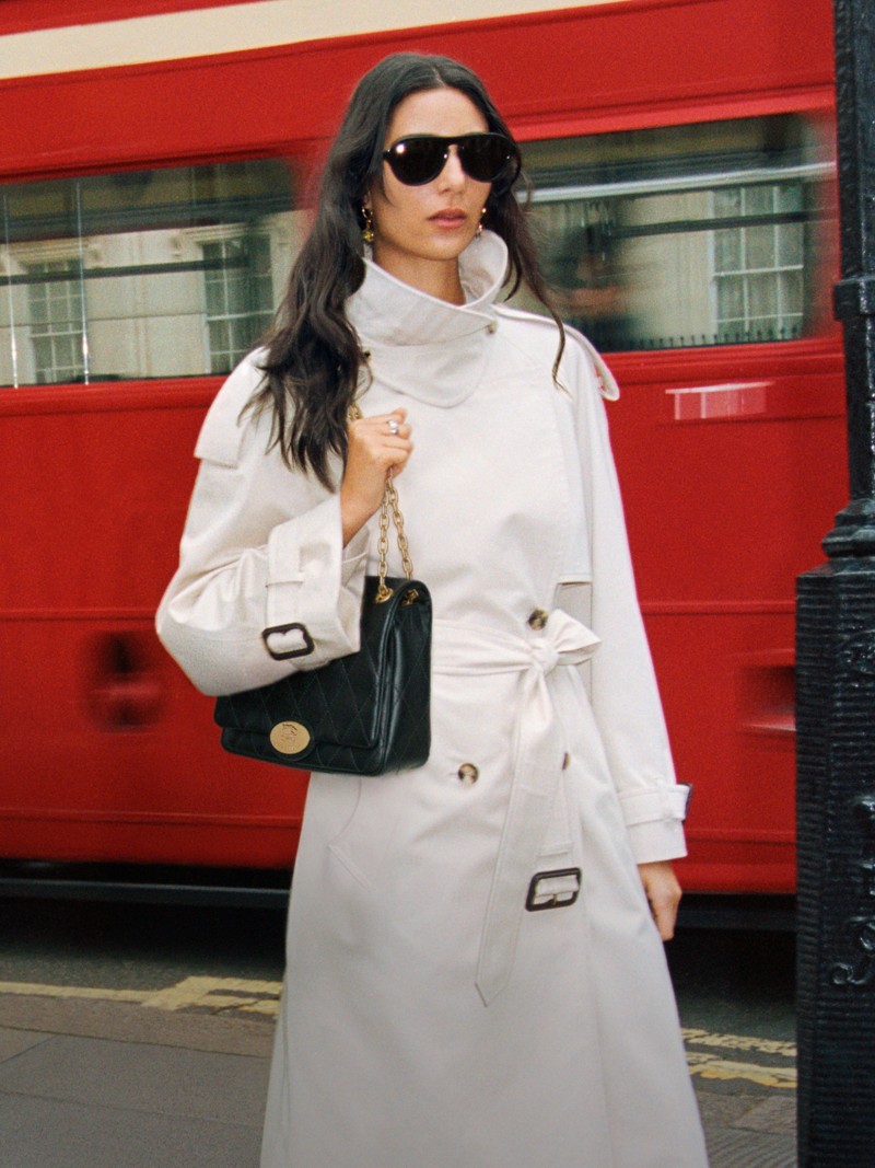 Model stood in front of London Red Bus, holding Black Strand Clutch Bag