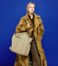 Modella che indossa un cappotto patchwork in shearling con camicia a righe, pantaloni in denim e tote Shield Twin in pelle