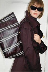 Shot of model wearing Short Gabardine Fitzrovia Trench Coat in colour Red Wine, holding Medium Highlands Tote in colour Mahogany red