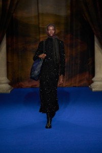 Assa Baradji wearing sequin-embellished dress and cavalier boots in black, intarsia leather Highlands shoulder bag in midnight blue, gold-plated Shield Segment ring and wool silk scarf in wine red.