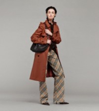 Model wearing Trench Coat in Rust paired with Silk Blouse and Burberry Check Trousers, holding Medium Shield Twin Bag