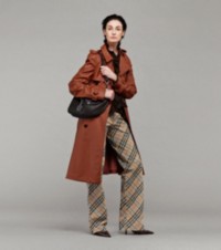 Model in Trenchcoat in der Farbe Rust, Seidenbluse und Hose im Burberry Check-Karomuster, mit mittelgroßer Tasche „Shield Twin“