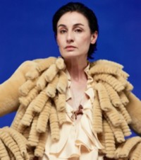 Modella con giacca in shearling con frange color fieno abbinata a una camicetta in seta con arricciature color Pelican