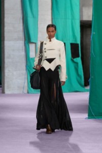 Model wearing cutout jacket in white, with a nylon jersey vest in black and maxi skirt in black.