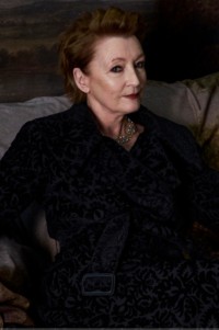 Lesley Manville vestindo trench coat de veludo na cor Vine e body de malha com padronagem texturizada em relevo