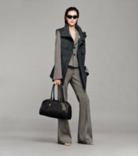 Modelo usando um colete cinza-carvão com paletó e calças de alfaiataria, segurando uma bolsa baú Shield Twin 