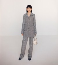 Modella che indossa giacca sartoriale in lana jacquard con motivo a quadri Principe di Galles in bianco e nero, abbinata alla borsa Knight piccola in pelle soap.