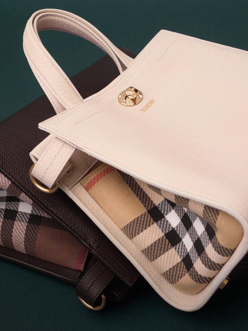 Dos bolsos Cotswolds en marrón y beige, con detalle de panel House Check sobre fondo verde oscuro.