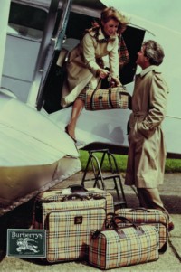 Werbung für Burberry aus dem Archiv, das ein reisendes Paar mit Gepäckstücken im Burberry Check und einem Flugzeug im Hintergrund zeigt 