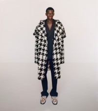 Mannequin portant une cape plaid à motif pied-de-poule noir et blanc, ainsi qu'une veste et un pantalon de costume noir et blanc en laine.