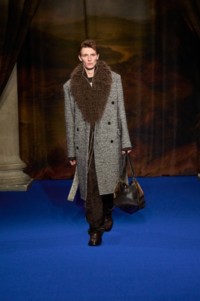 Finnlay Davis wearing faux fur wool cashmere tailored coat in rice beige and raven grey, sunflower jacquard shirt and trousers in hawk brown, leather ledger boots in treacle brown and intarsia leather highlands bowling bag in hazel brown.