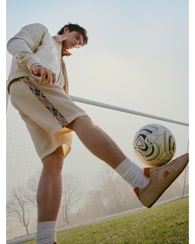 Shot of Actor Bright, kicking a football, wearing Suede Knight Runner Sneakers​ in colour Flax beige/pumpkin orange