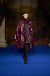 Wang Chen-Ming portant une parka en fausse fourrure coloris rouge Mahogany, un gilet intérieur en nylon matelassé à imprimé rouge Sherry, un pull à col roulé en marron Walnut, un pantalon de costume en marron Soot, des bottes Cavalier en cuir marron Treacle et des boucles d'oreilles Shield argentées.