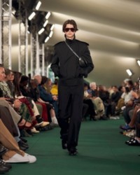 O modelo está usando uma jaqueta trench com calças de alfaiataria e loafers Shield.