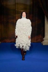 Lina Zhang wearing crochet fringed cape in and waffle-knit sweater in white, Herringbone cotton jodphurs in wine red, paired with thigh high boots in mahogany red and Gold Star earrings and Gold-plated Spear Pavè ring.