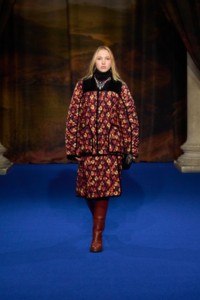 Lila Moss wearing leaf print jacket and quilted skirt in poppy red, leather Cavalier boots in conker brown and Gold-plated Charm hoop earrings and Silver-plated enamel Star Bow necklace. 