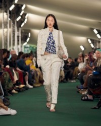 A modelo está usando uma jaqueta com bordado floral, blusa com estampa de morangos e calças com bordado floral.