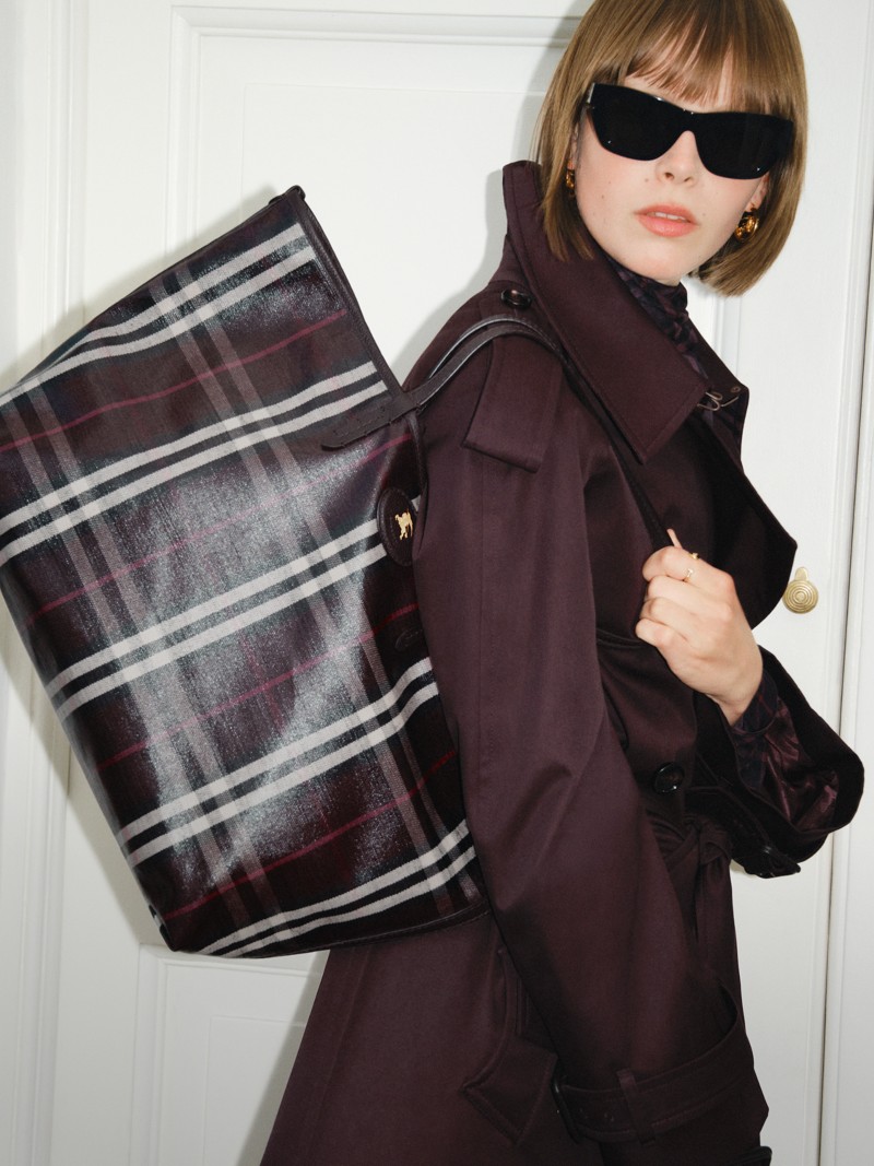 Shot of model wearing Short Gabardine Fitzrovia Trench Coat in colour Red Wine, holding Medium Highlands Tote in colour Mahogany red