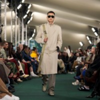 라지 쉴드 크로스바디 백과 트렌치코트를 착용한 모델.