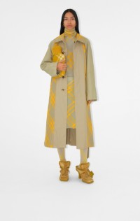 Mulher vestindo um trench coat longo e segurando uma bolsa de água quente amarela
