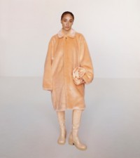 Modella che indossa cappotto in pelliccia sintetica peach e pochette Rose in pelle verniciata peach.