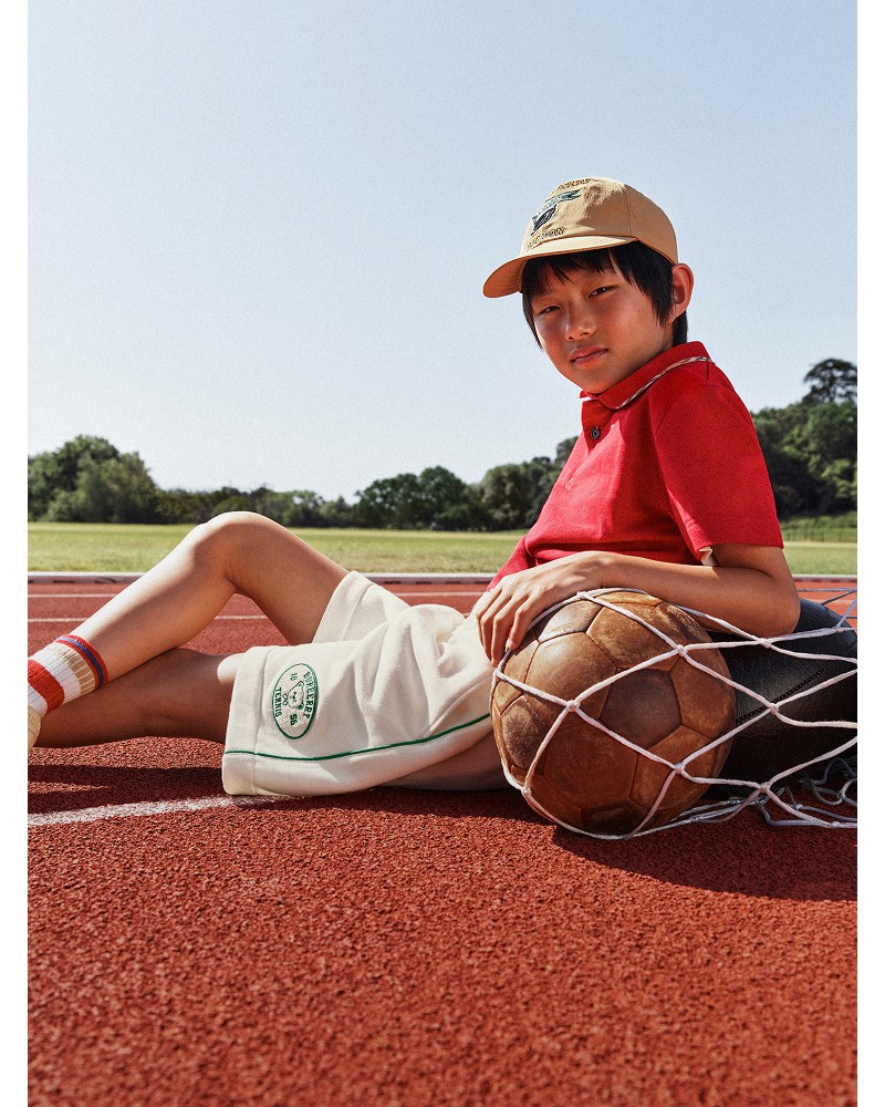 Shot of model wearing Boys' Polo Shirt in colour Bright Red and Varsity Cap in Sand