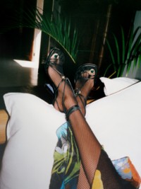 クッションにレザー アイビー シールド ヒールサンダルを履いた足を乗せた写真