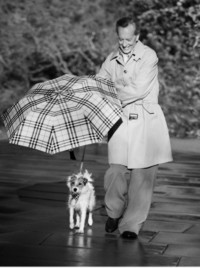 Richard E. Grant in einem Burberry-Trenchcoat und mit einem Regenschirm in Check beim Spazierengehen mit einem Hund für die Kampagne It's Always Burberry Weather