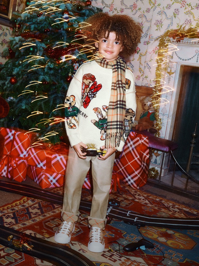 Burberry Festive Campaign featuring a child wearing a check burberry scarf and Thomas Bear and Friends Wool Blend Sweater surrounded by festive decoration and wrapped gifts.