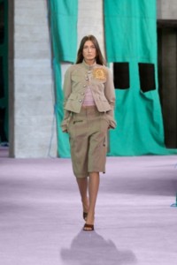 Model wearing canvas peplum jacket in quill, with a nylon jersey vest in wisteria and capri trousers in quill.