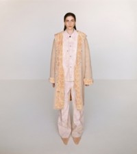 Modella che indossa cappotto con cappuccio e stampa rose, giacca in tela e pantaloni in cameo, abbinati a mule a punta in peach.