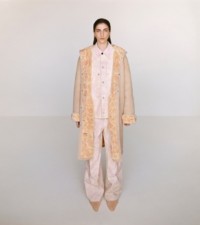 Modella che indossa cappotto con cappuccio e stampa rose, giacca in tela e pantaloni in cameo, abbinati a mule a punta in peach.