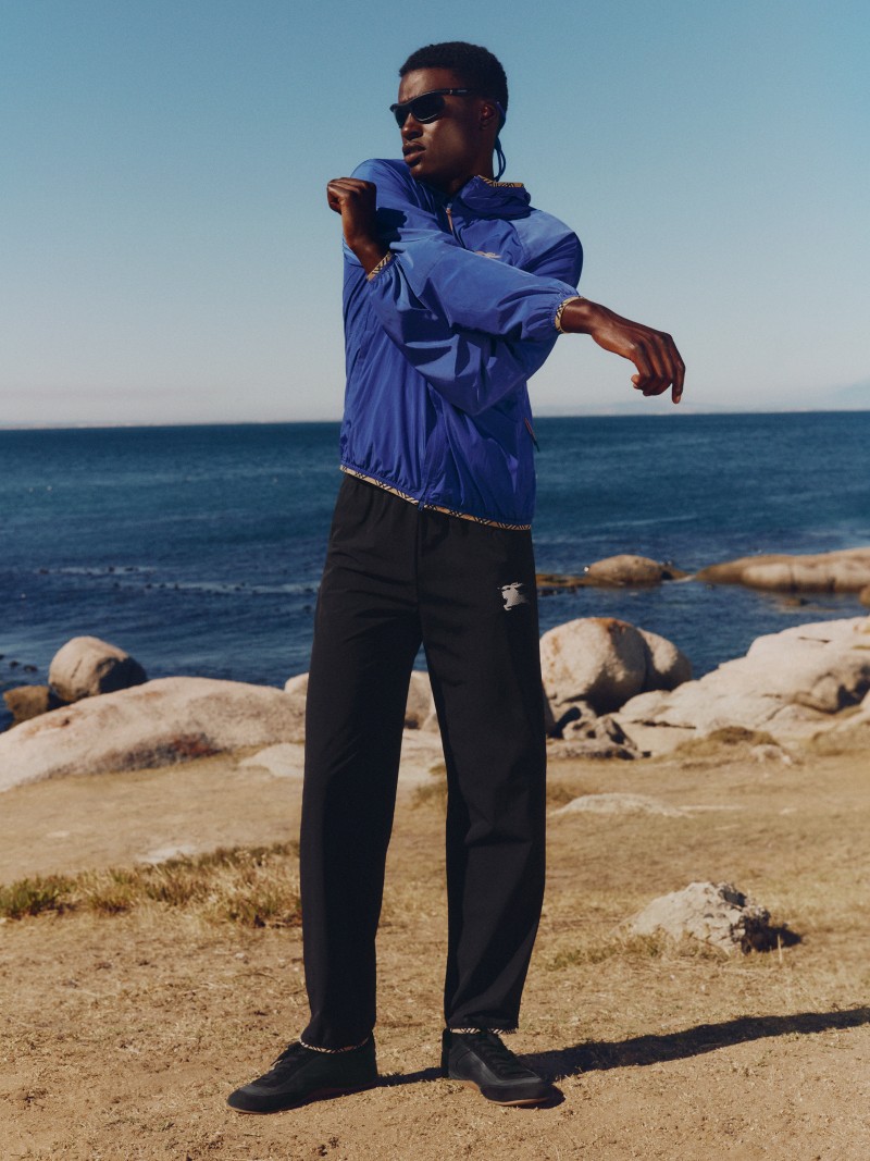 Modelo que luce una chaqueta ligera azul y pantalones deportivos negros con detalles Check para la campaña de prendas deportivas de Burberry. 