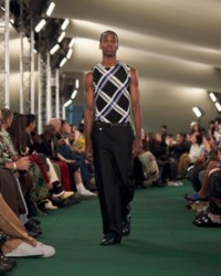 O modelo está usando uma blusa xadrez em ponto canelado e calças de alfaiataria.