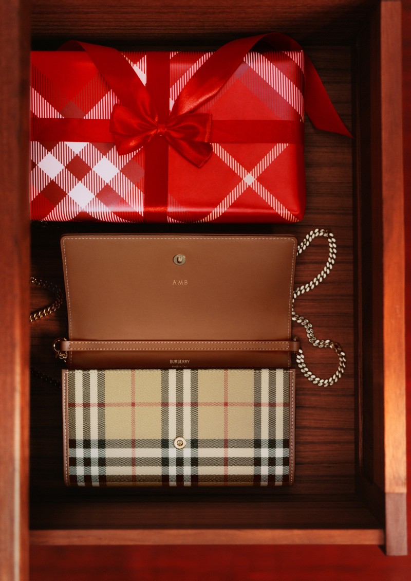 Burberry Festive Campaign featuring the Check Chain Strap Wallet next to a gift wrapped in Burberry check wrapping and a red bow. 