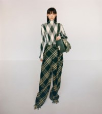 Modella che indossa maglia a collo alto in seta e cotone con motivo Argyle in ivy e sherbet, abbinata a pantaloni con pieghe e motivo Check sfumato in primrose.